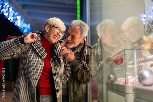 Elderly husband and wife shopping during holiday season holding hands and laughing while looking at store window.