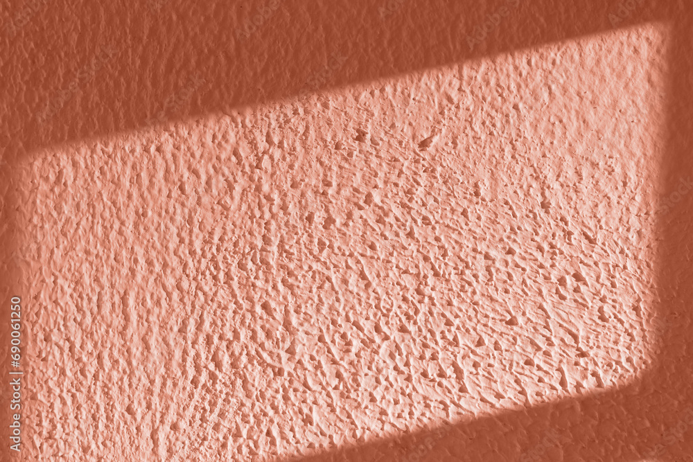 Fototapeta premium Textured peach color wall bathed in soft light, casting linear shadows.