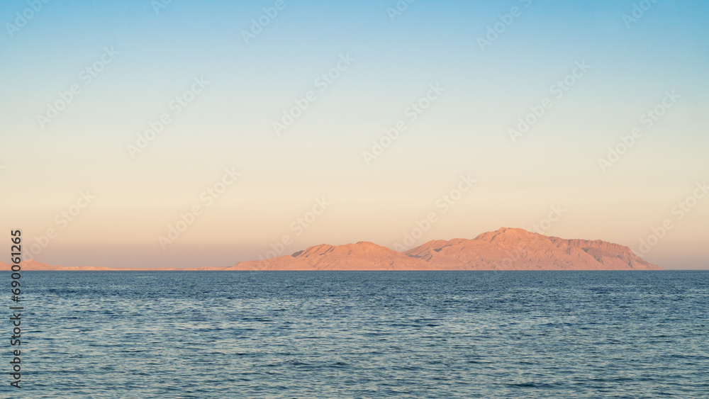 Serene seascape at dusk with gentle waves and a clear view of distant mountains under a soft sky.