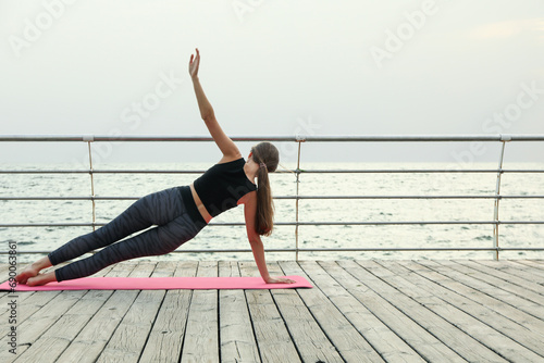 Young woman on yoga mat on wooden floor outdoors, space for text