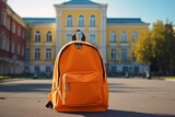 Orange backpack in front of the modern school building. Back to school concept