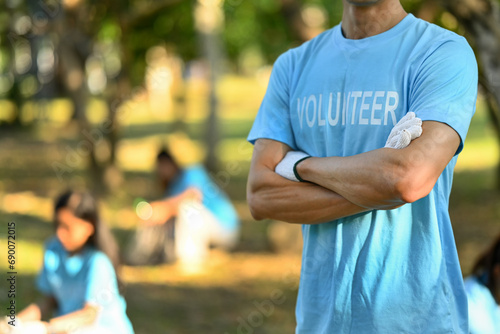Man in volunteer uniform standing with arms crossed while standing outdoor. Charity and community service concept © Prathankarnpap