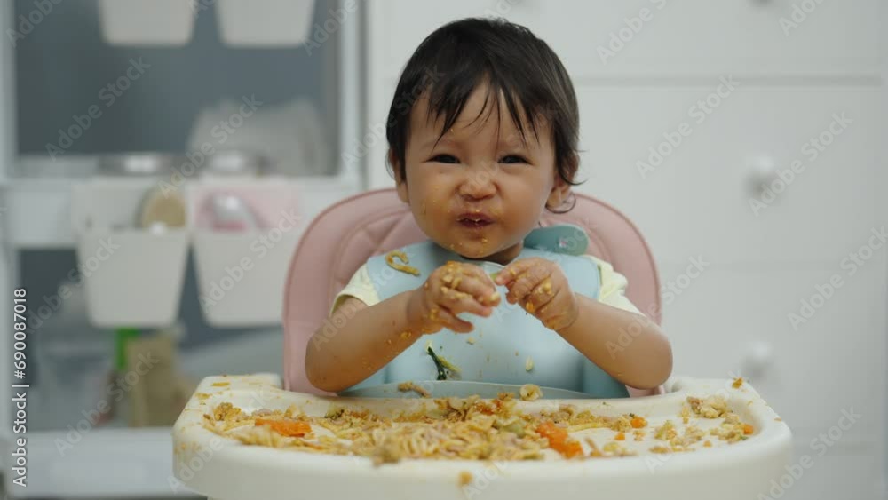 happy infant baby eating food and vegetable by self feeding BLW or baby led weaning on a chair happy infant baby eating food and vegetable by self feeding BLW or baby led weaning on a chair