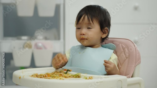 infant baby eating food and vegetable by self feeding BLW or baby led weaning on a chair photo