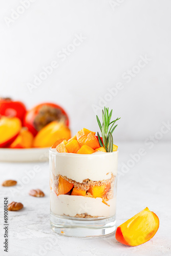 Trifle in a glasses with persimmon, rosemary, pecan, whipped coconut cream and biscuit on a table. Healthy food, vegan, sugar, gluten and lactose free.