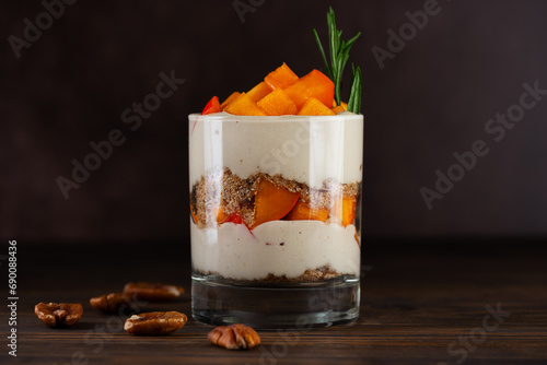 Parfait with persimmon, rosemary, pecan, whipped coconut cream and biscuit on a brown. Healthy food, vegan, sugar, gluten and lactose free.