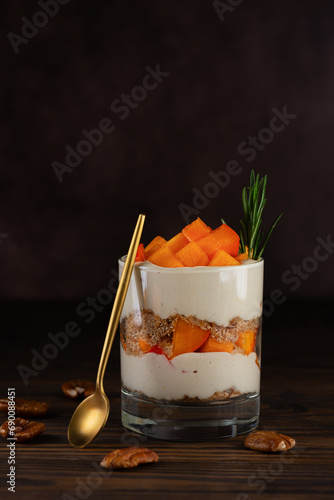 Trifle with persimmon, rosemary, pecan, whipped cream and biscuit on a brown table. Healthy food, vegan, sugar, gluten and lactose free.