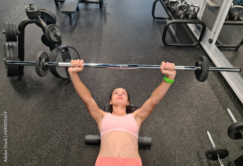 Foto Woman pressing barbell while lying on bench in gym