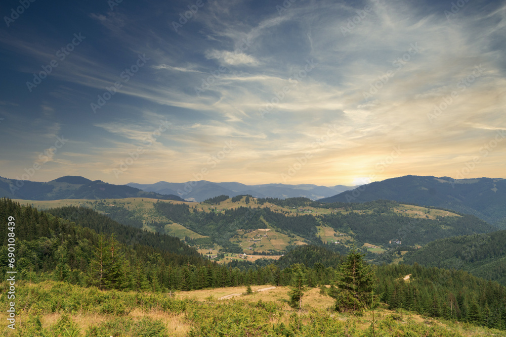 Panoramic view of rolling hills with forest under a blue sky at sunset.