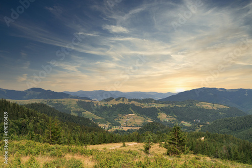 Panoramic view of rolling hills with forest under a blue sky at sunset.