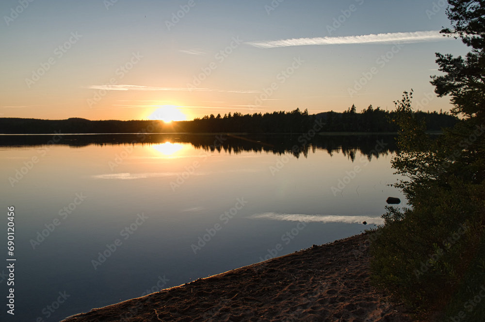Sunset with reflection on a Swedish lake in Smalland with bushes in the foreground Sunset with reflection on a Swedish lake in Smalland with bushes in the foreground