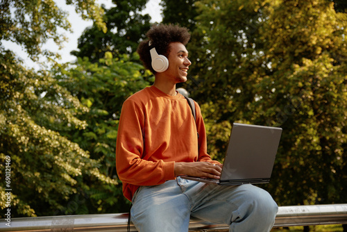 Happy smiling male student wearing wireless headphones using laptop