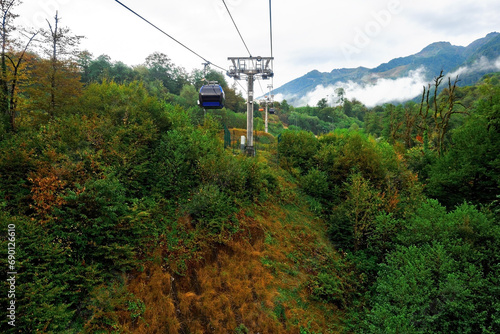 Cable car with cabin in mountains. Funicular. Sightseeing route or excursion for tourists in mountains on cloudy summer day.
