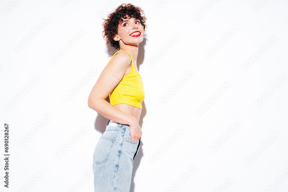 Young beautiful smiling female in trendy summer yellow tank top. Carefree woman posing near white wall in studio with curly hairstyle. Positive model having fun, going crazy. Cheerful and happy Young beautiful smiling female in trendy summer yellow tank top. Carefree woman posing near white wall in studio with curly hairstyle. Positive model having fun, going crazy. Cheerful and happy