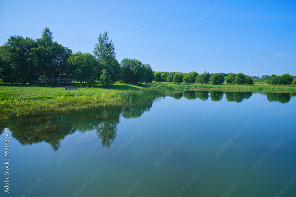 The blue water of a clear lake with a reflection of the sky and green trees