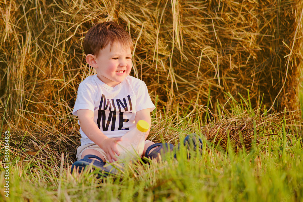 Baby with bottle milk is having fun on the farm with hay stacks, as the summer sun set. Portrait of a happy kid aged two years Baby with bottle milk is having fun on the farm with hay stacks, as the summer sun set. Portrait of a happy kid aged two years