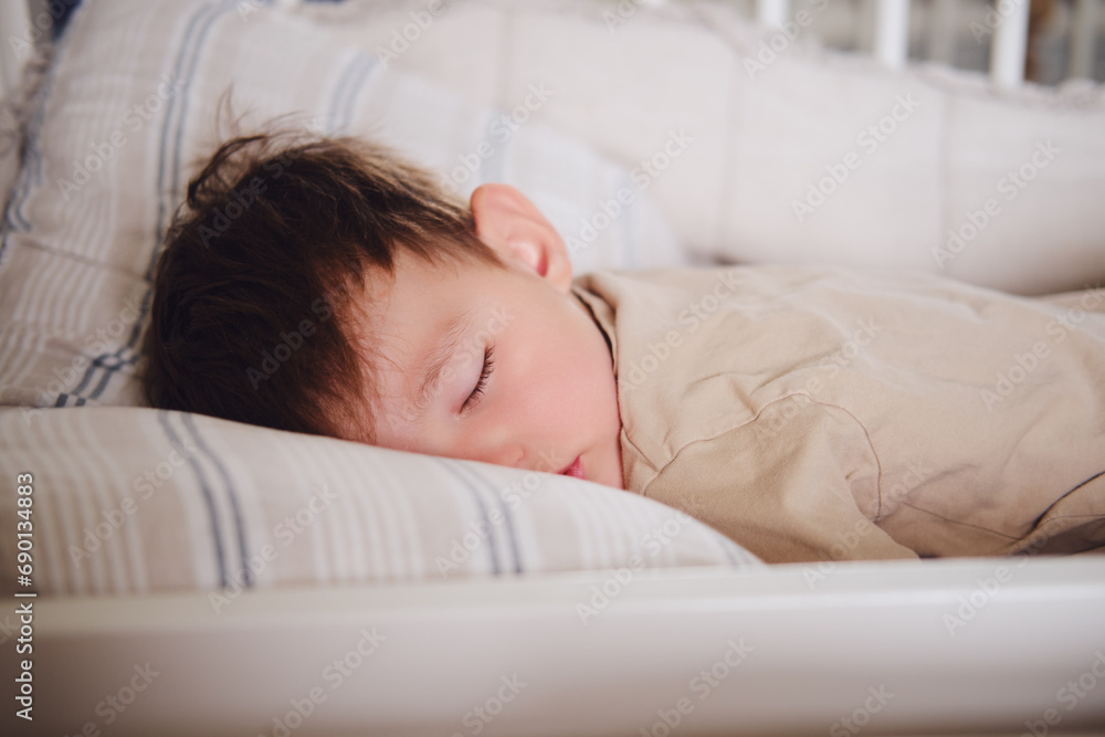 The two-year-old toddler baby is sleeping in his crib. Child boy is sleeping on a pillow in bed. Kid aged two years The two-year-old toddler baby is sleeping in his crib. Child boy is sleeping on a pillow in bed. Kid aged two years