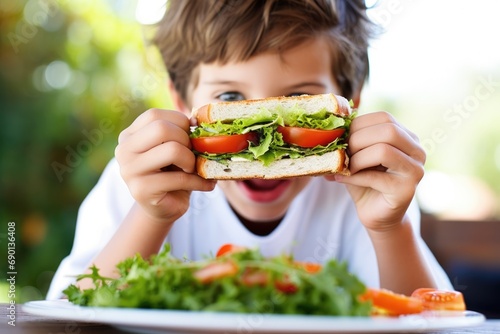 a child eating a humongous sandwich with fresh herbs photo