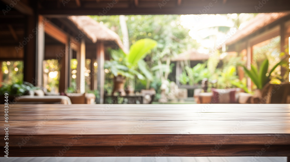 An empty wooden table foregrounds a blurred Balinese-style interior, inviting a serene and tropical atmosphere perfect for a calm setting. - obrazy, fototapety, plakaty 