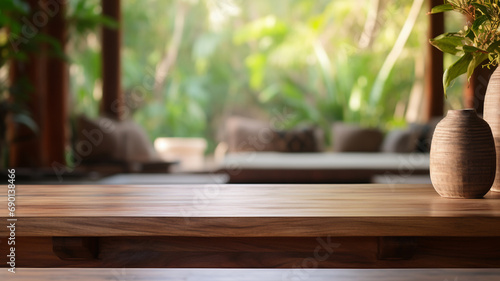 An empty wooden table foregrounds a blurred Balinese-style interior, inviting a serene and tropical atmosphere perfect for a calm setting. © Alina Nikitaeva