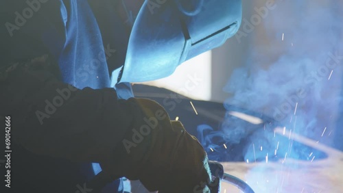 Closeup tilt shot of unrecognizable workman wearing welding helmet welding machinery using blowpipe at heavy machinery production plant photo