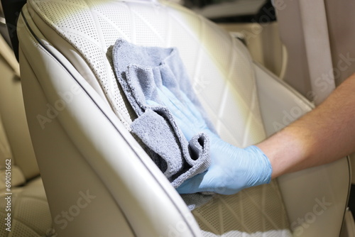 A man cleaning leather car seat with microfiber cloth. Dry cleaning of the car interior, close-up, selective focus. Detailing and car cleaning services, the concept of car washing and cleaning. photo