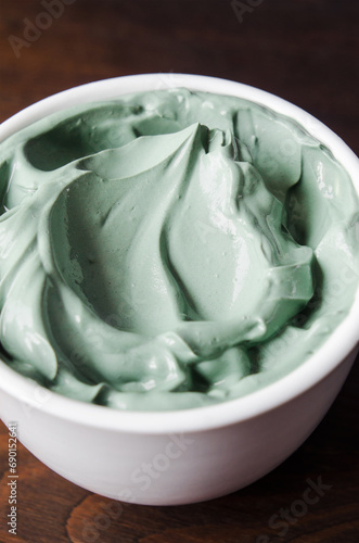 Green (blue) bentonite clay facial mask in a small white bowl. Homemade natural beauty treatment and spa recipe. Clay texture close-up.