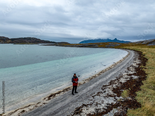 young man taking a selfie from a drone on the coast of mjelle beach of norwegian with blue cyan water and mountains on background