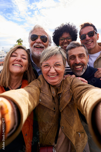 Cheerful vertical selfie of a group of mature people looking at camera happily, taking photos during their family trip together. photo