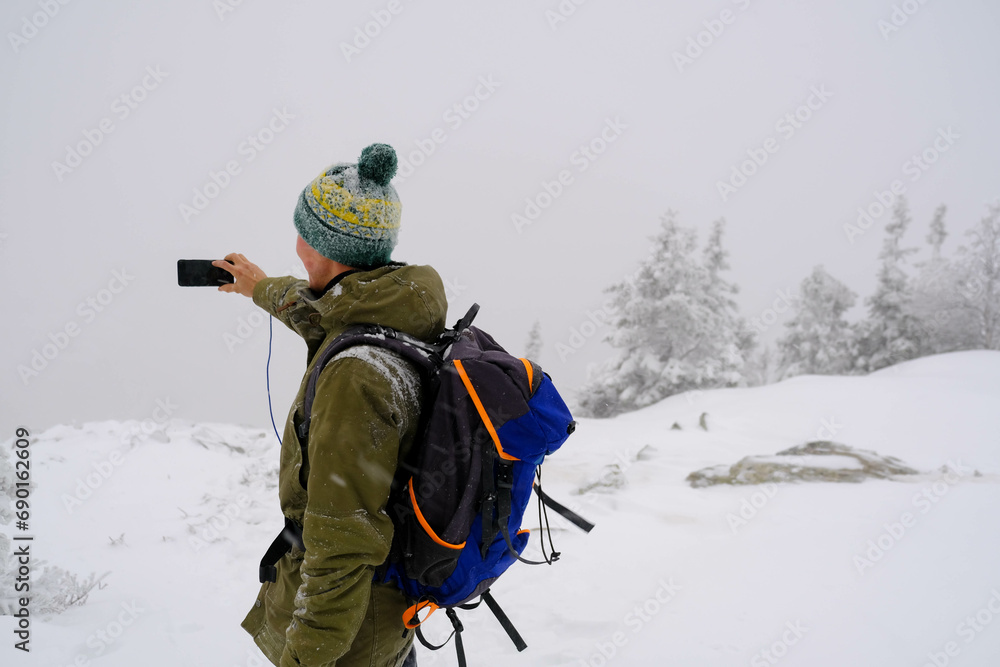 a tourist with a backpack climbed to the top of the mountain in winter and takes pictures of the landscape