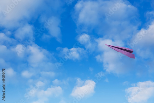 Purple paper plane flying in blue sky with clouds