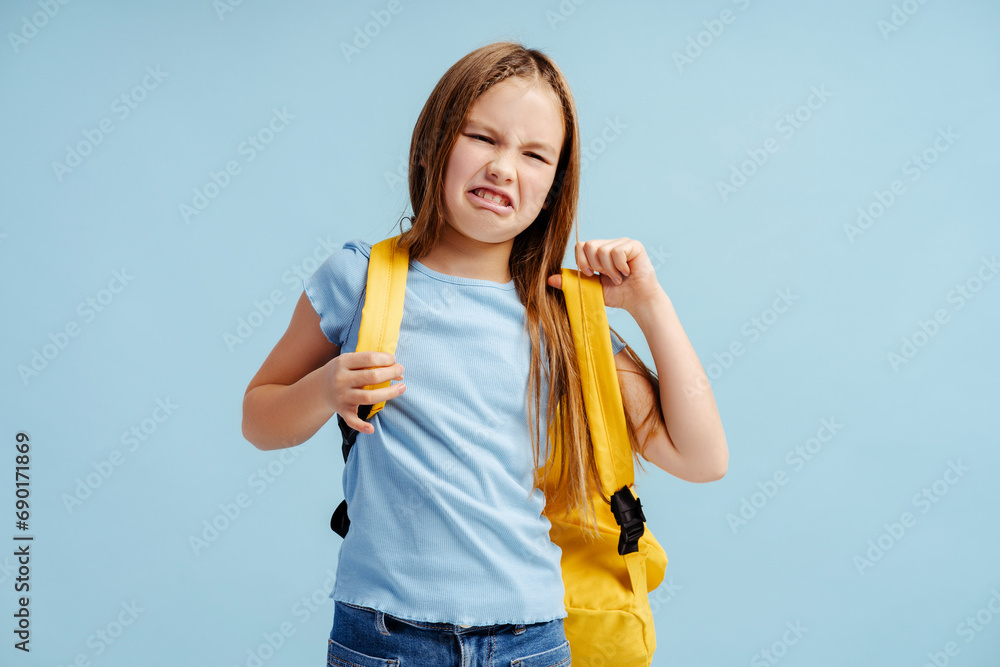 Upset crying little girl, pupil wearing casual clothes backpack isolated on blue background Upset crying little girl, pupil wearing casual clothes backpack isolated on blue background
