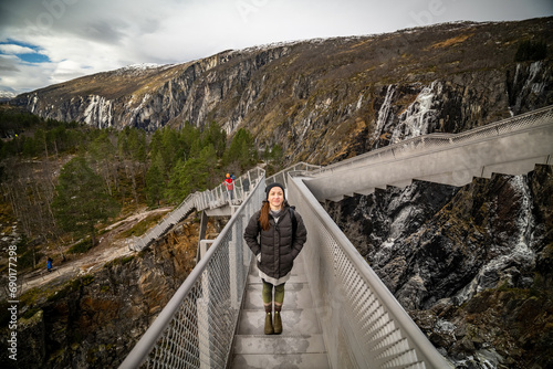 young beautiful woman watching and smiling in camera on bridge over Vøringfossen watefall in norway photo