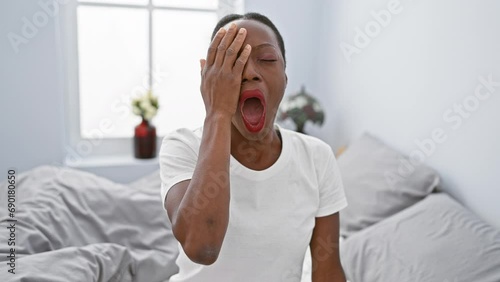 Exhausted african american woman in bedroom, fatigue covering half her face, hand on mouth, yawning tiredly photo