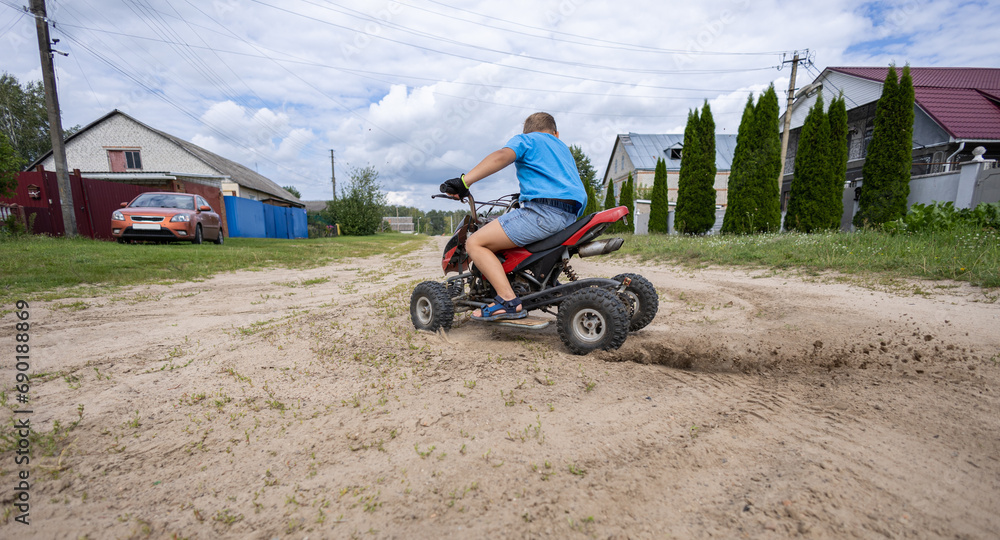 A child makes a sharp turn on an ATV, kicking up dust and sand from the road. The wheels of the ATV slip on the sand, raising dust and sand. A child boy enjoys riding an ATV. A child makes a sharp turn on an ATV, kicking up dust and sand from the road. The wheels of the ATV slip on the sand, raising dust and sand. A child boy enjoys riding an ATV.