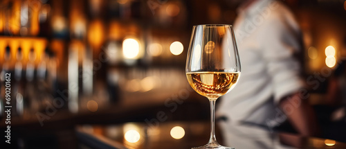 close up of a glas of white wine with blurred Bartender and bar in the back with empty copy space © Uwe