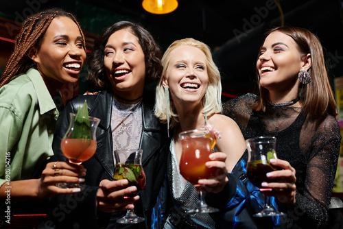glamorous multiethnic girlfriends with delicious cocktails laughing while having fun in bar