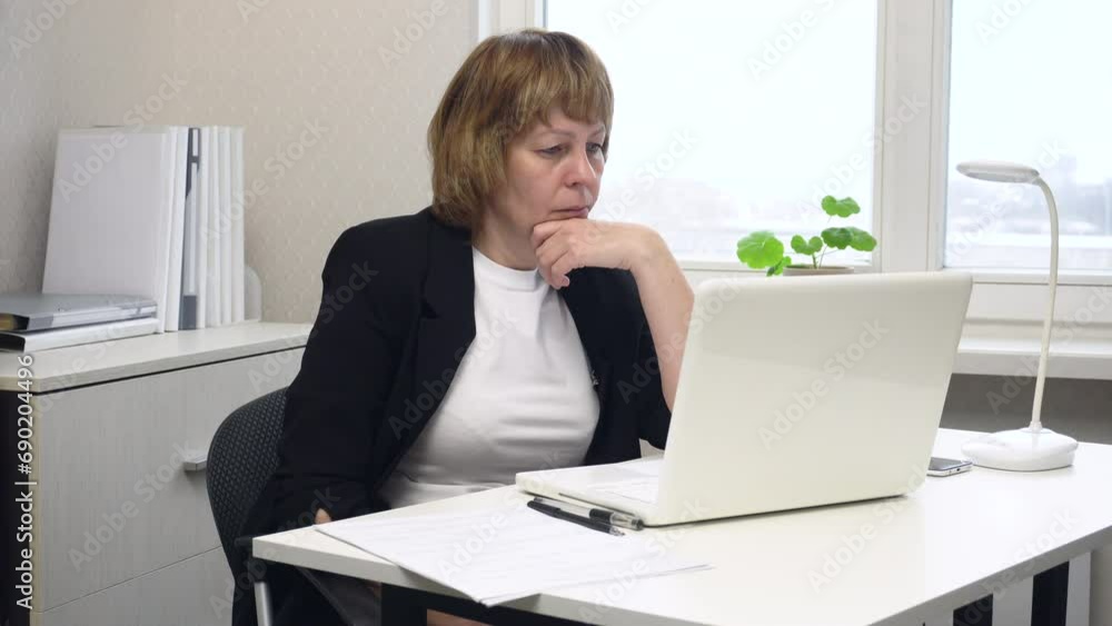 A woman sits at a table in the office and intently studies information on the monitor screen. The video is suitable for content about sales strategies, remote work, office organization and time manage A woman sits at a table in the office and intently studies information on the monitor screen. The video is suitable for content about sales strategies, remote work, office organization and time manage