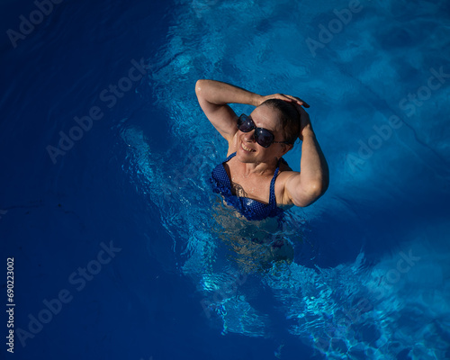 An elderly woman in sunglasses swims in the pool. Vacation in retirement. 