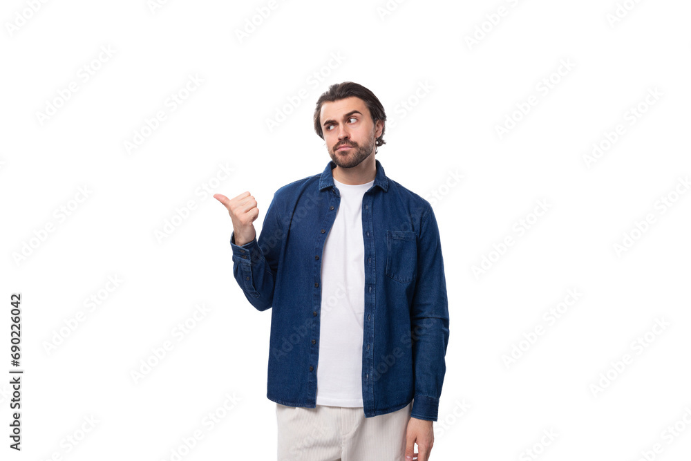 handsome well-groomed young brunette man in a denim shirt points his hand to the side handsome well-groomed young brunette man in a denim shirt points his hand to the side