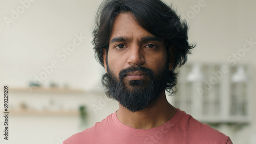 Close up front view adult 30s multiracial Arabian Indian ethnic bearded man serious looking at camera. Male head shot portrait of calm middle-aged muslim guy homeowner home renter posing alone indoors photo