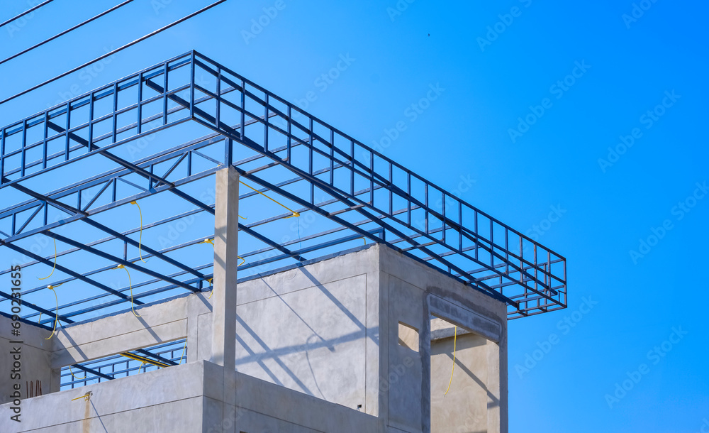 Incomplete precast bare concrete room wall with electric conduit wiring system on roof beam outline on top of modern office building structure in construction site against blue sky background Incomplete precast bare concrete room wall with electric conduit wiring system on roof beam outline on top of modern office building structure in construction site against blue sky background