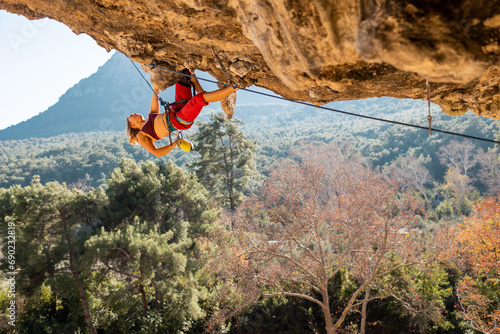 Girl climber on an overhanging rock. A sports woman climbs a rock against the backdrop of mountains. difficult movements in rock climbing.