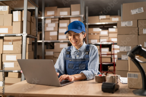 Employee in retail shop's warehouse. Small Business Owner working on laptop, preparing and packing parcels for delivery. photo