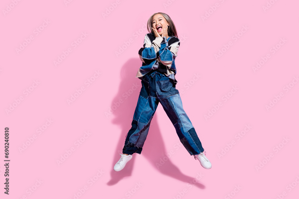 Full size photo of adorable lovely girl dressed jeans pullover oversize pants flying hands on cheeks isolated on pink color background