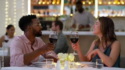 Couple in restaurant with wine, conversation and toast at table, valentines day or interracial romance. Fine dining, drinks and cheers, happy man and woman relax on luxury dinner date with smile. photo