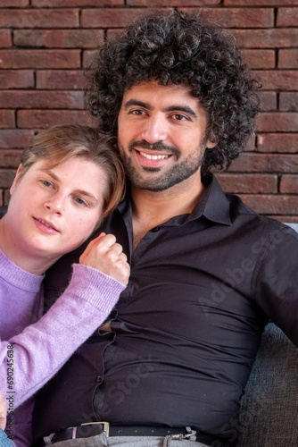 This image portrays a cozy biracial moment between two people sharing a comfortable embrace. A person in a lilac sweater leans on a man with curly hair, their closeness indicative of a strong bond