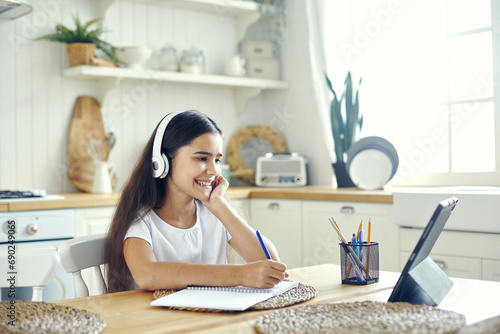 Preteen 12s girl in wireless headphones sit at table e-learning photo