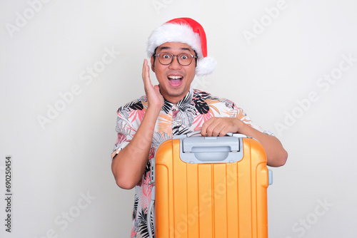 A man wearing christmas hat holding luggage with wow face expression photo