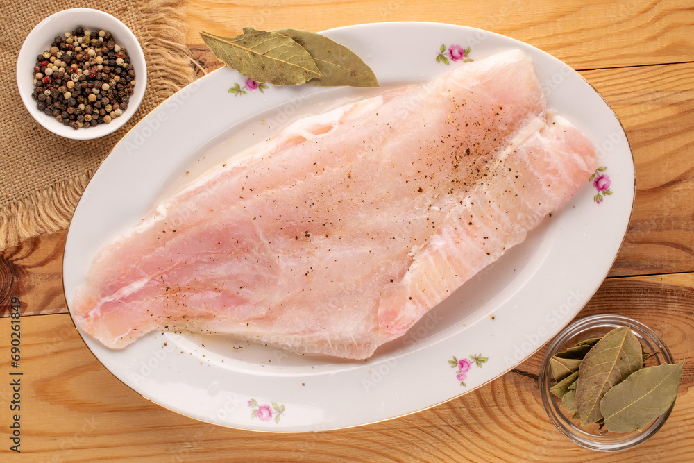 Raw cod fillet with spices on a ceramic plate, macro, top view Raw cod fillet with spices on a ceramic plate, macro, top view